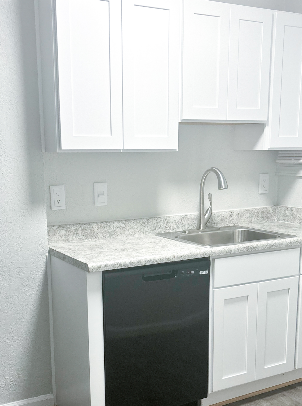 A kitchen with white cabinets and a black dishwasher