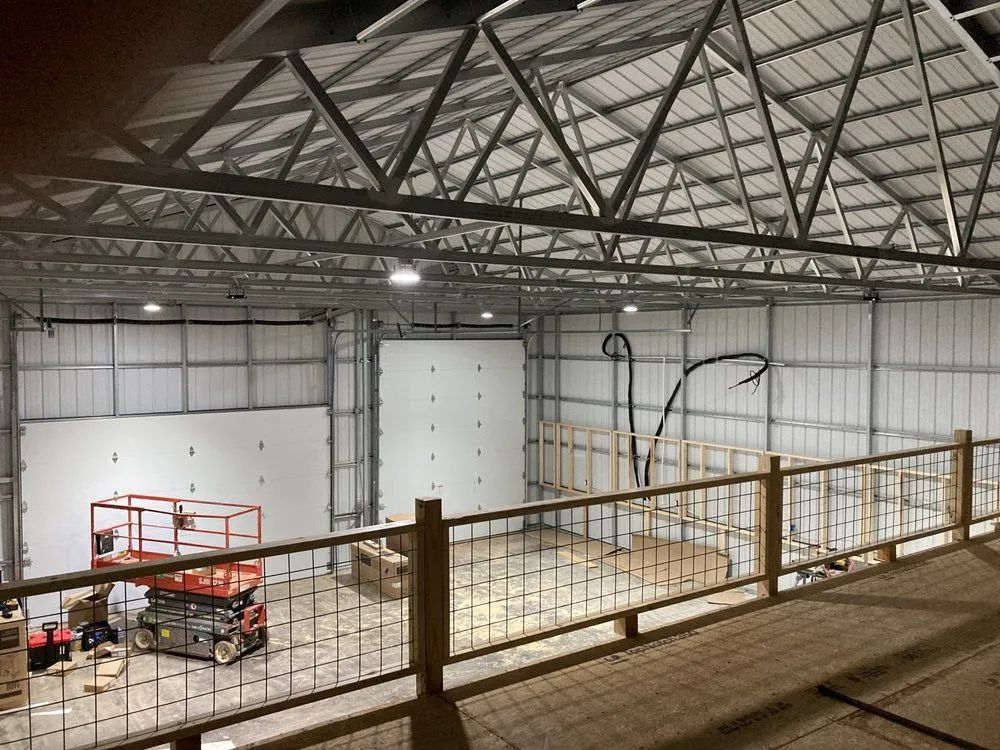 Interior of a large warehouse-style building with metal beams and walls, a lift, and a wooden railing.