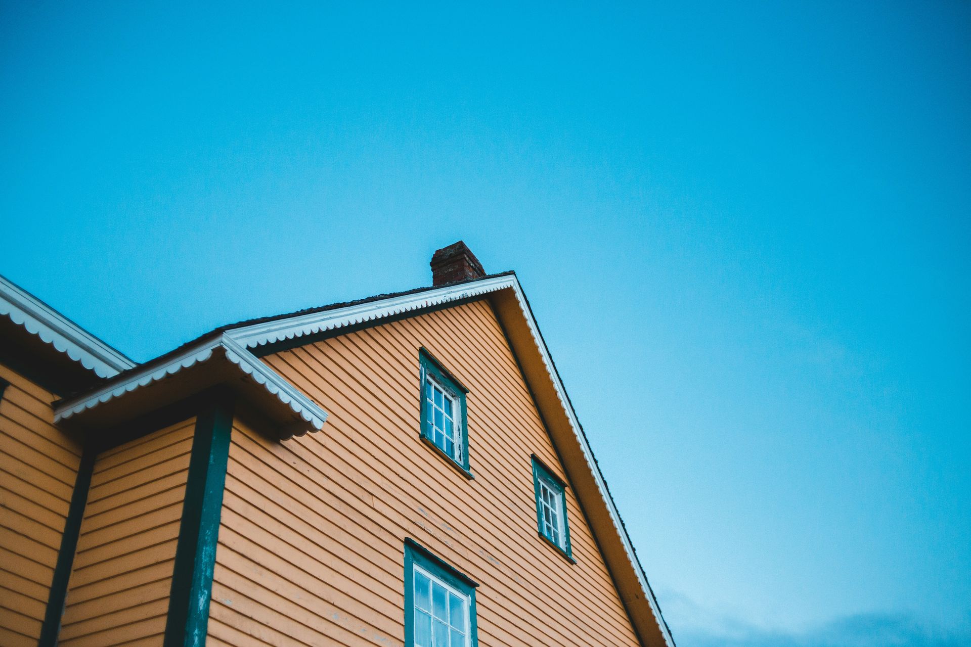 a yellow house with green windows and a blue sky in the background .