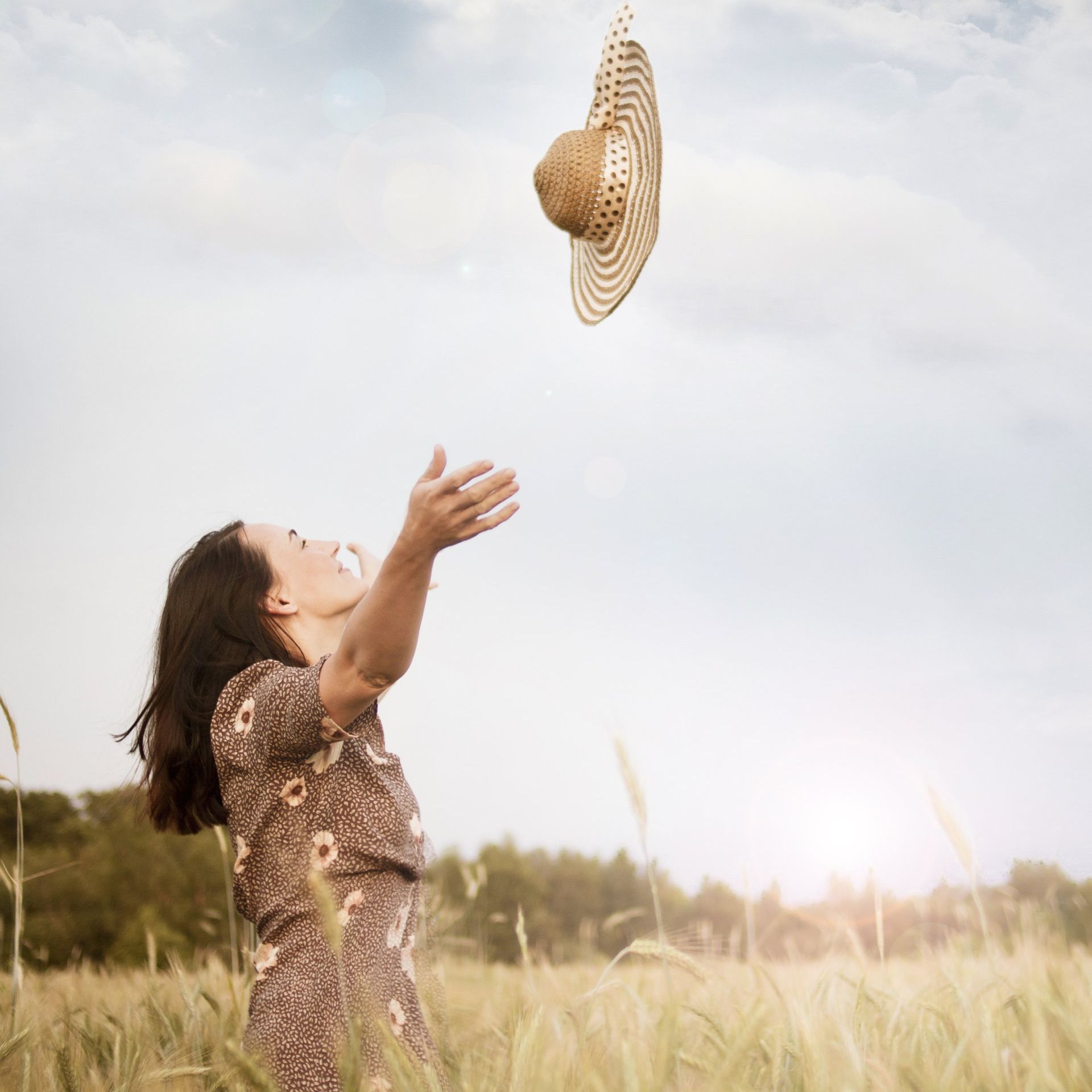 woman in wheat field tossing her straw hat into the air