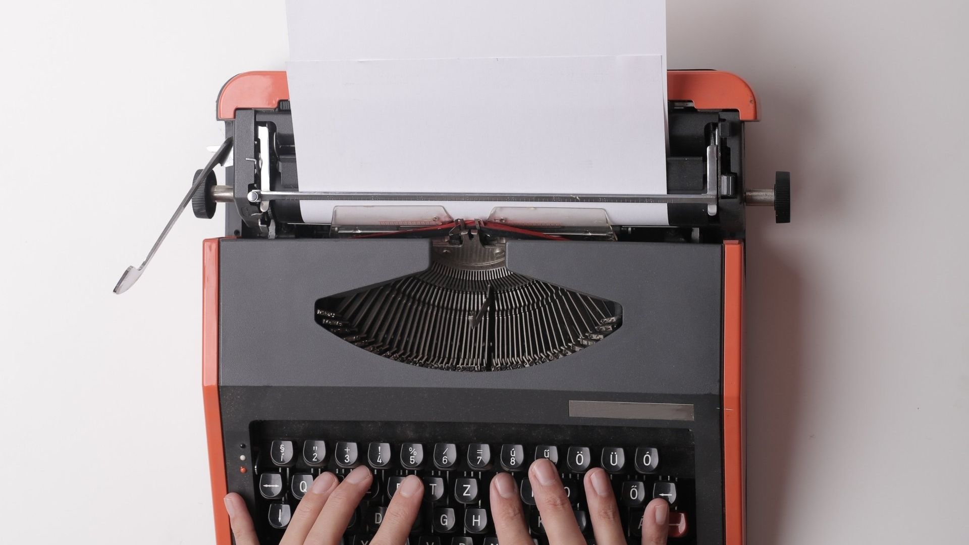 orange typewriter with hands on keys and empty paper loaded
