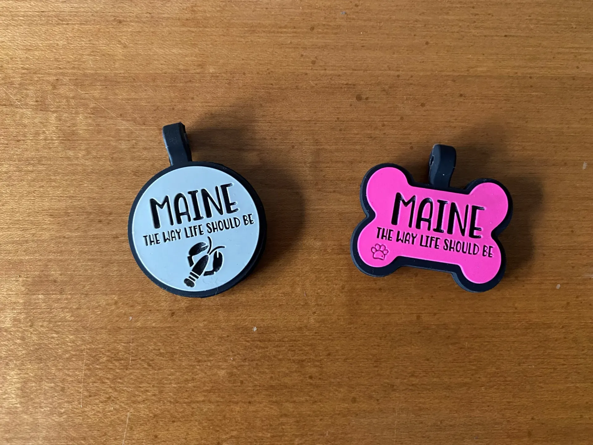 Two dog tags with the name maine on them are sitting on a wooden table.