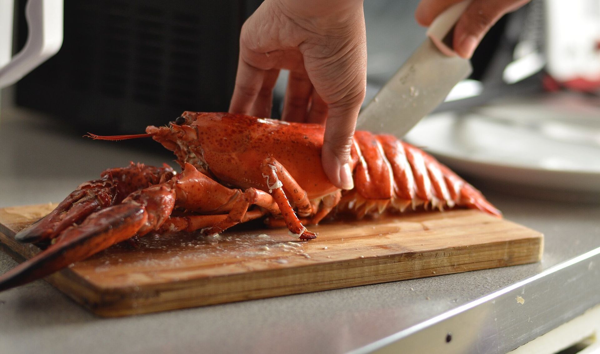 A person is cutting a lobster on a cutting board.