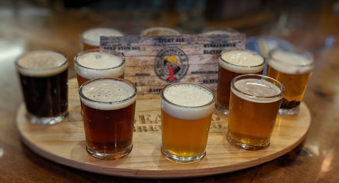 A wooden tray filled with different types of beer on a table.