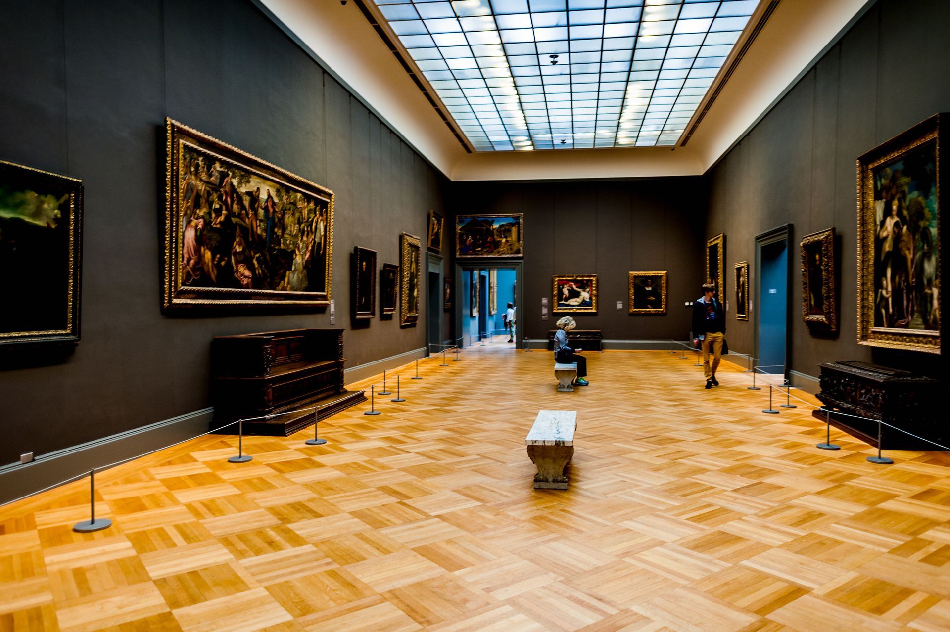 A man is walking through a museum filled with paintings.