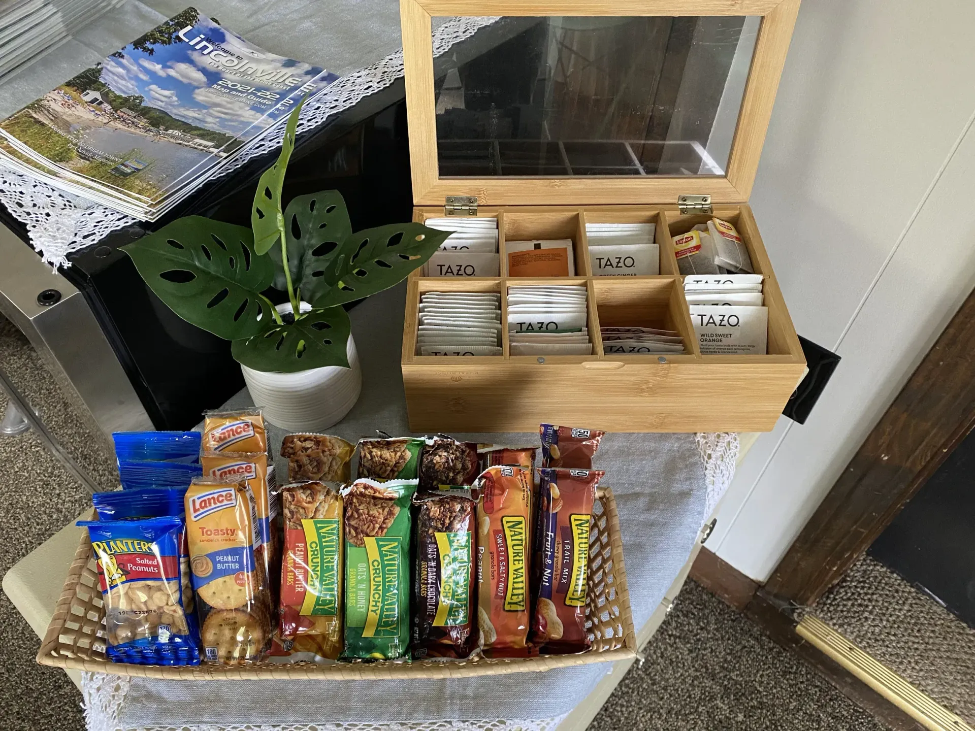 A wooden box filled with tea and snacks is on a table next to a basket of snacks.