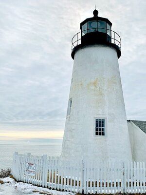 A white lighthouse is surrounded by a white picket fence.