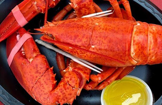 A lobster is sitting on a black plate next to a container of butter.