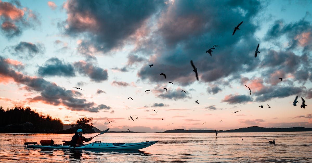 A person is paddling a kayak on a lake at sunset.