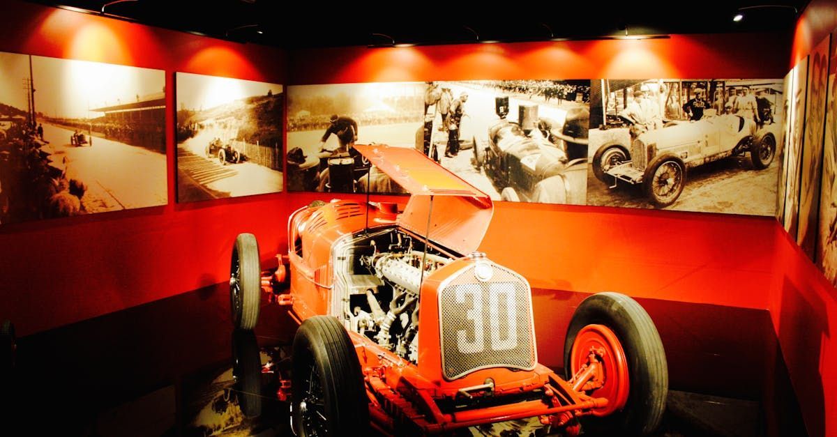 A red race car with the number 30 on the front is sitting in a room with pictures on the wall.