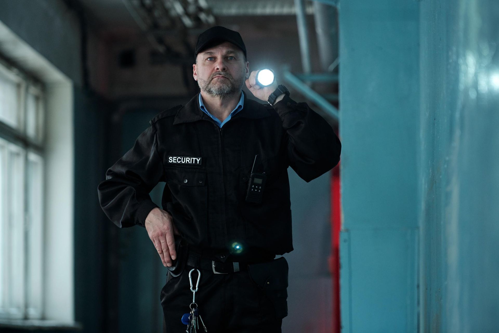 Security guard with flashlight in a hallway, wearing a black uniform and cap.
