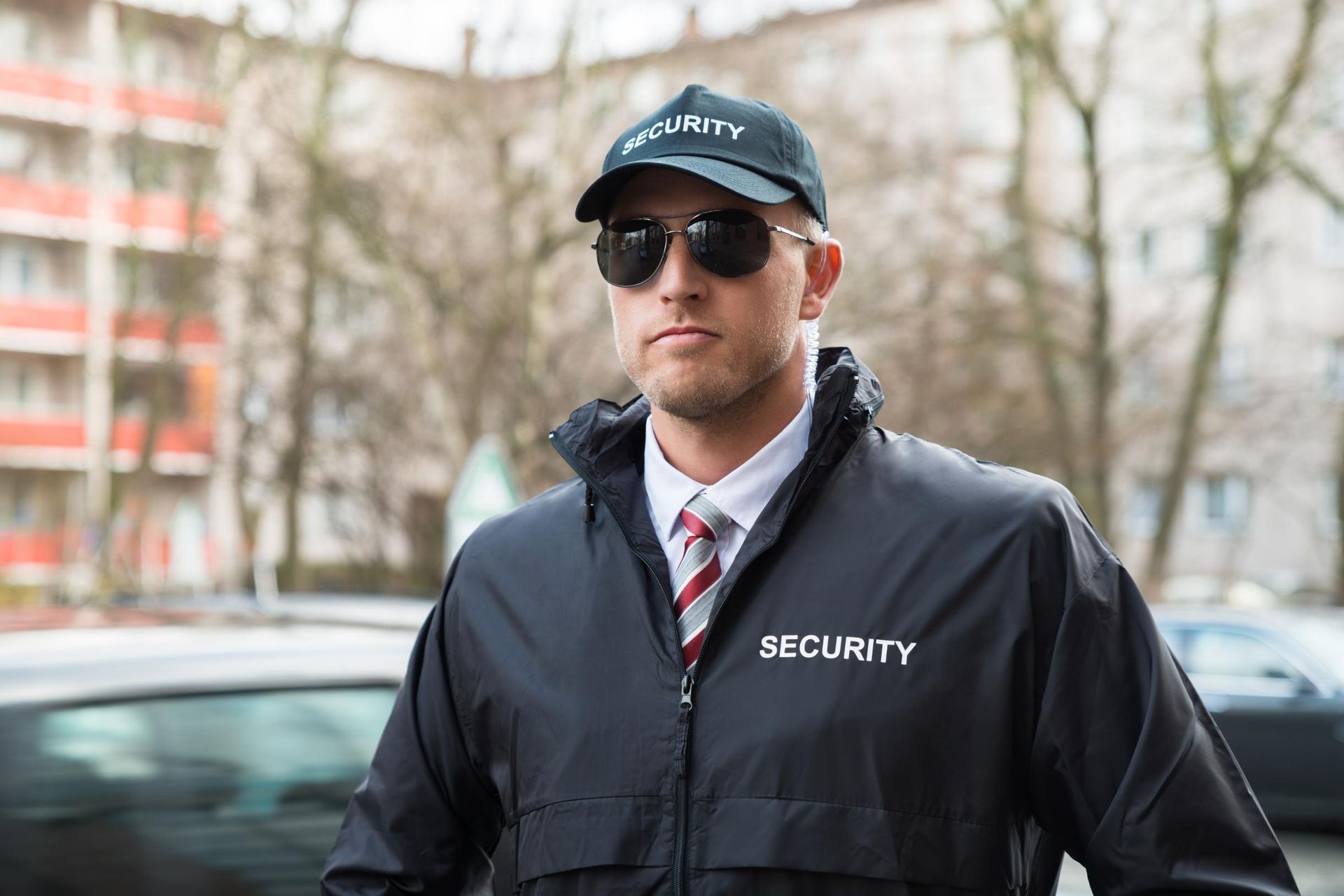 Security guard in black uniform and sunglasses, standing outdoors.