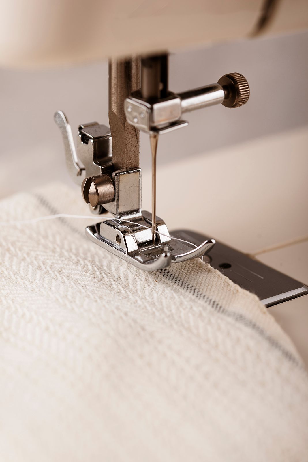 La aguja de la máquina de coser desciende sobre la tela blanca que se sujeta bajo el prensatelas metálico.