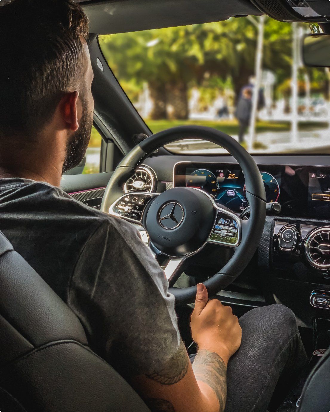Man driving a Mercedes-Benz. Interior shot with focus on the steering wheel, dashboard, and the driver's tattooed arm.