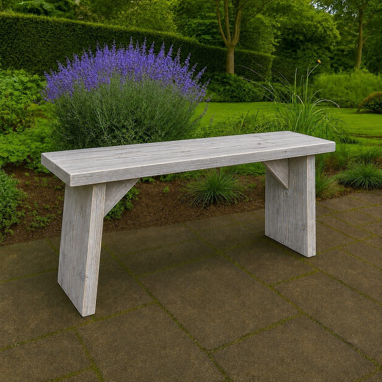 Een grijs bankje op een geplaveid pad naast een groene tuin met paarse bloemen.