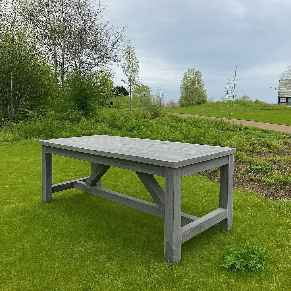Grijze houten tuintafel in een grasrijk park met bomen en een pad op de achtergrond.