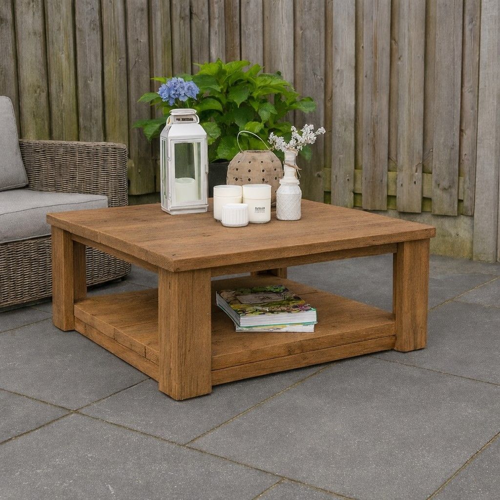 Bruin houten salontafel met lantaarn, kaarsen, bloemen en boeken op een grijs stenen terras.