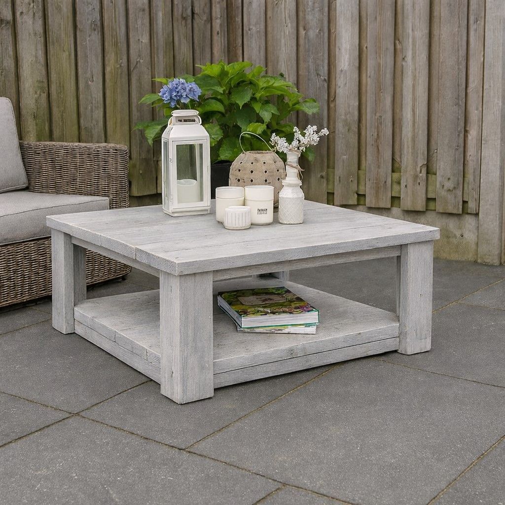 Grijze salontafel voor buiten met lantaarn, kaarsen, bloemen en tijdschriften op een terras naast een rieten stoel.