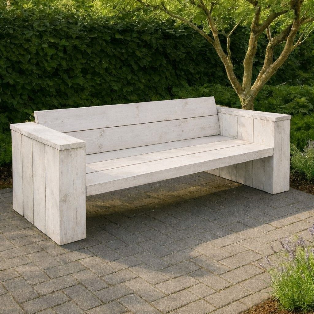 Witte buitenbank van hout op een betegeld terras naast groene hagen.