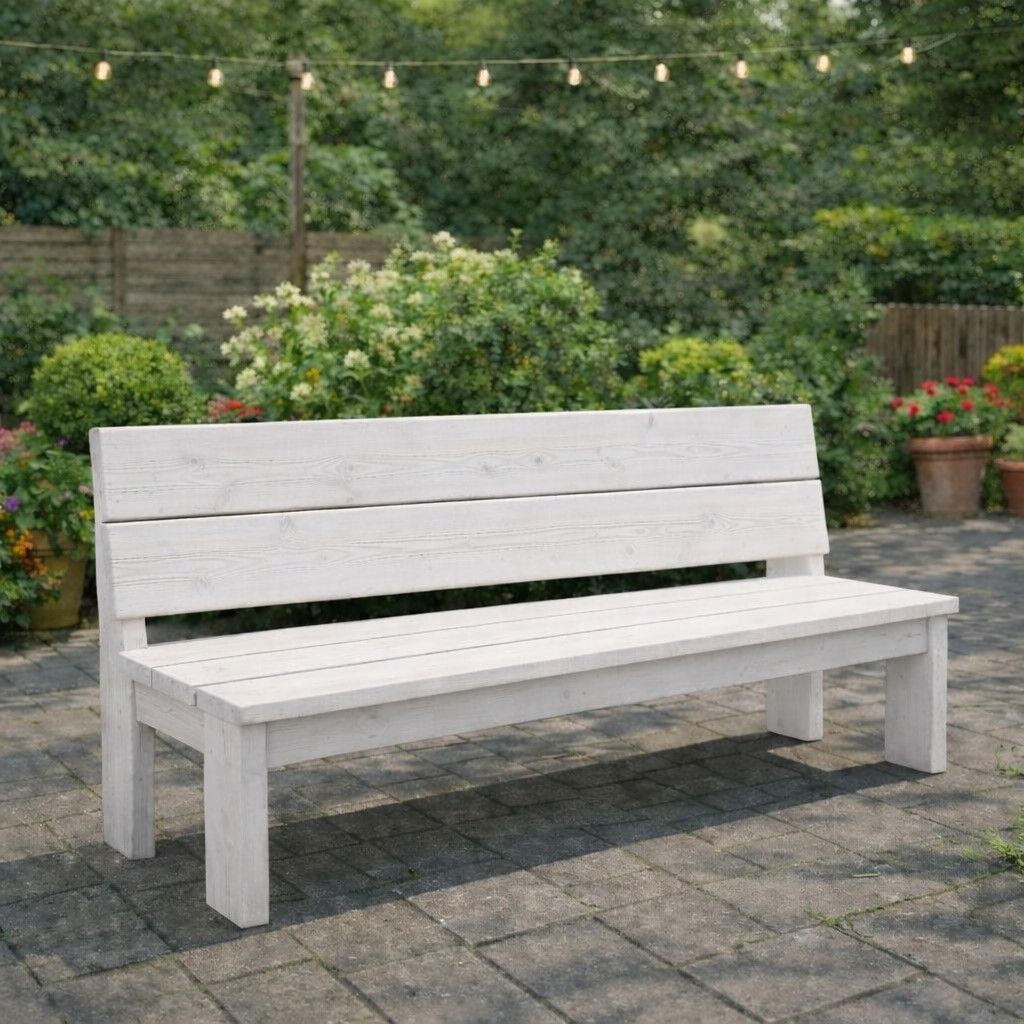 Witte houten bank op een stenen terras in een tuin met groen en lichtslingers.