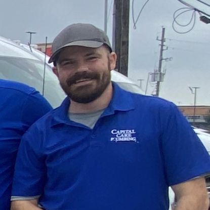 A man with a beard is wearing a blue shirt and a hat.