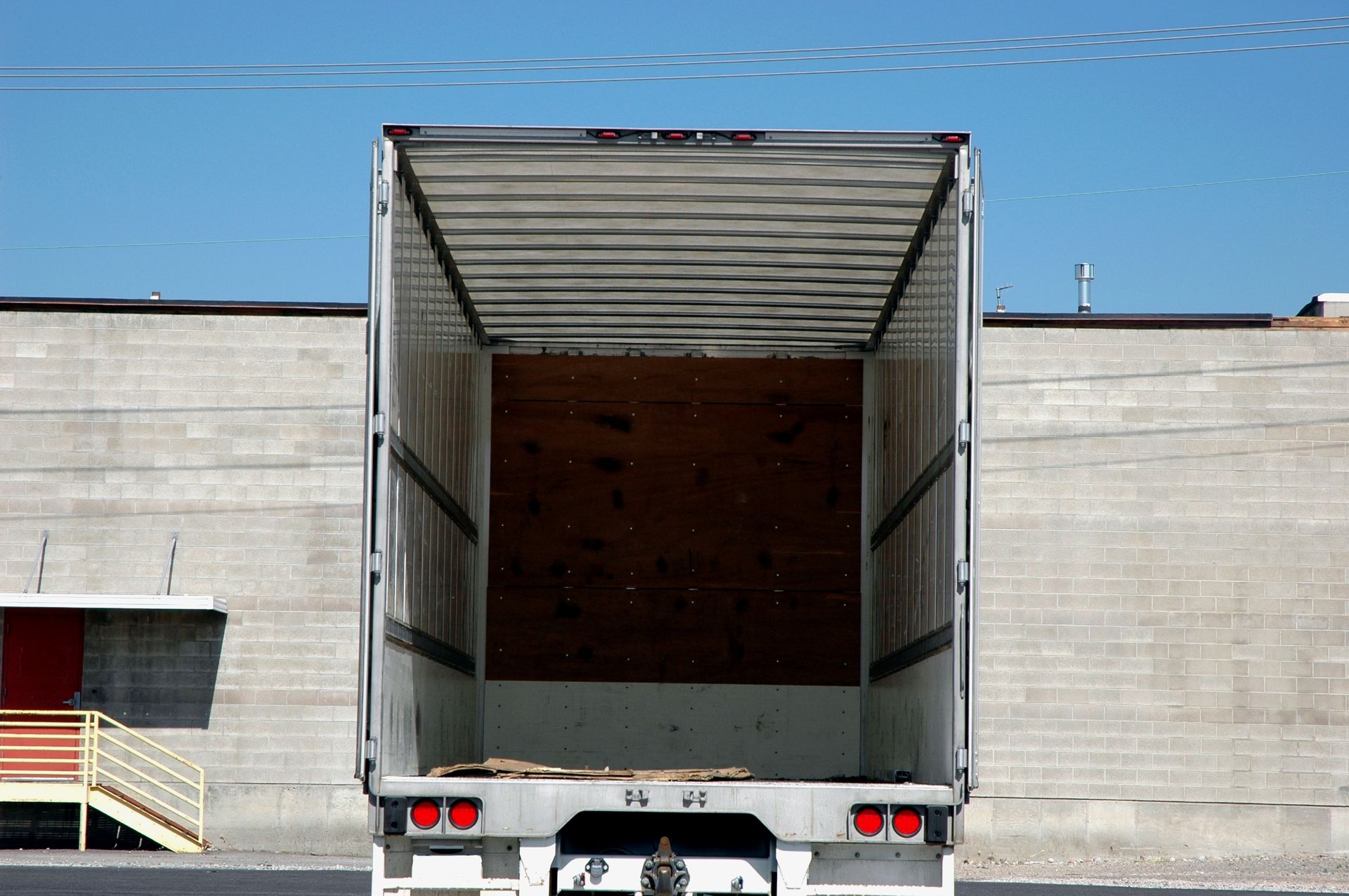 Open empty truck cargo area against a brick wall under a blue sky.