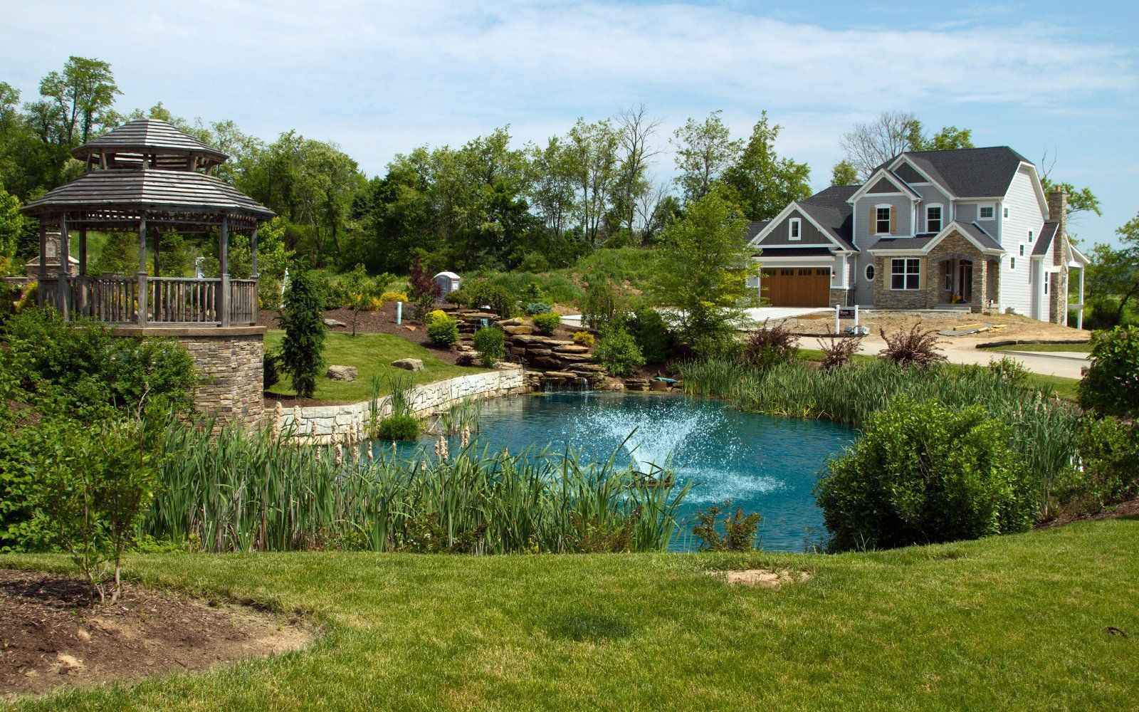 A house with a gazebo and a pond in front of it.
