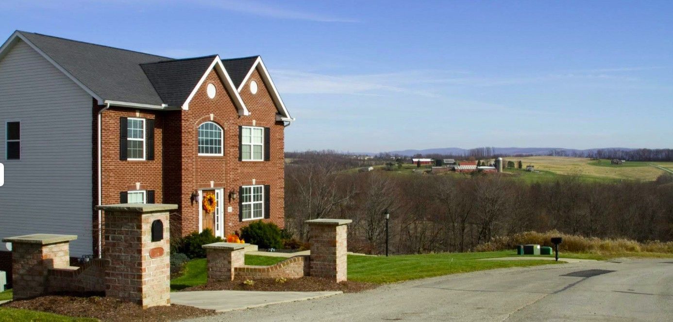 A large brick house with a gray siding is sitting on top of a hill.