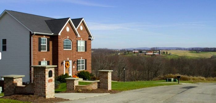 A large brick house with a gray siding is sitting on top of a hill.