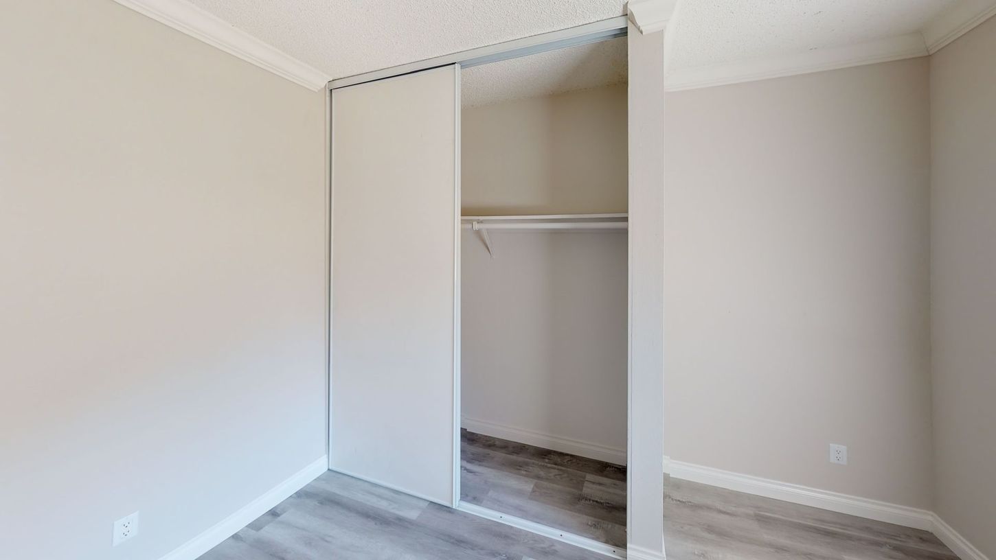 Empty closet with sliding doors, neutral walls, and a hanging rod.