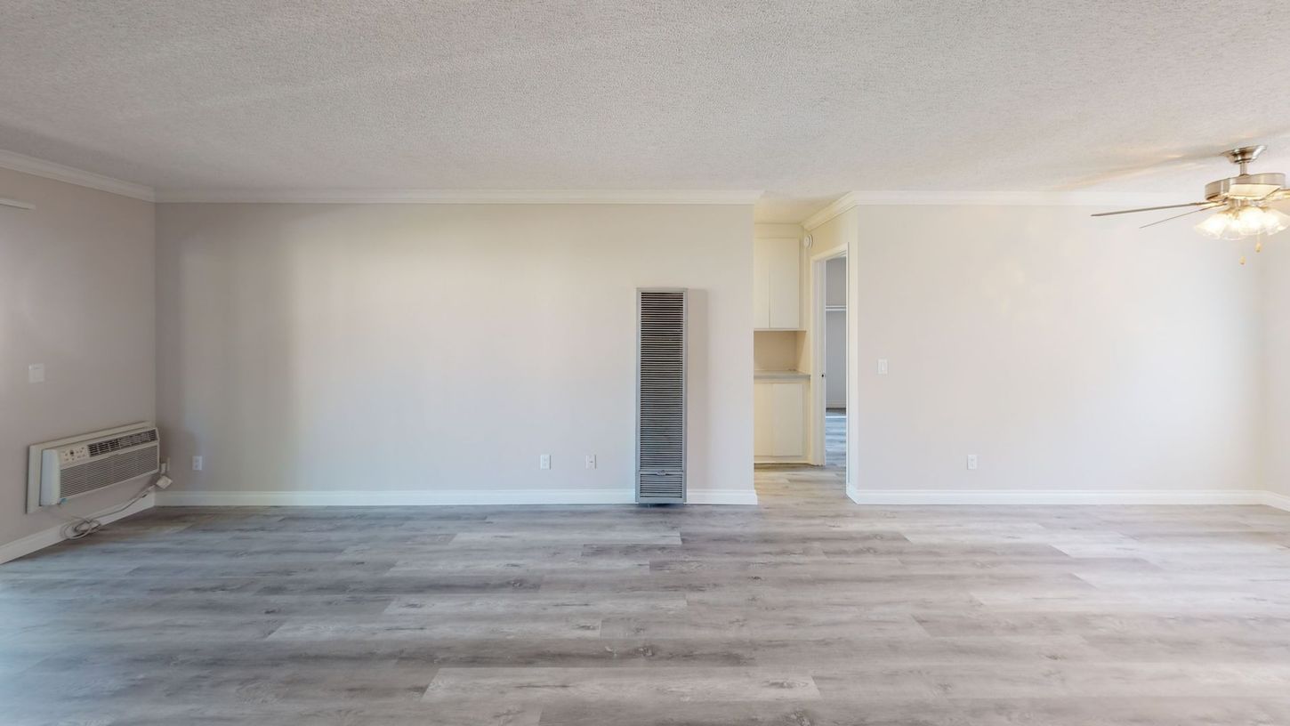 Empty living room with gray wood-look flooring, white walls, and a ceiling fan.