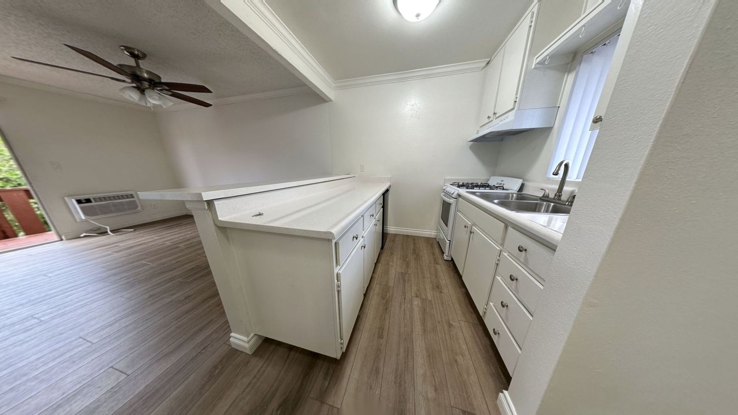 White kitchen with a large island and a stove. Hardwood floors and a ceiling fan are visible.