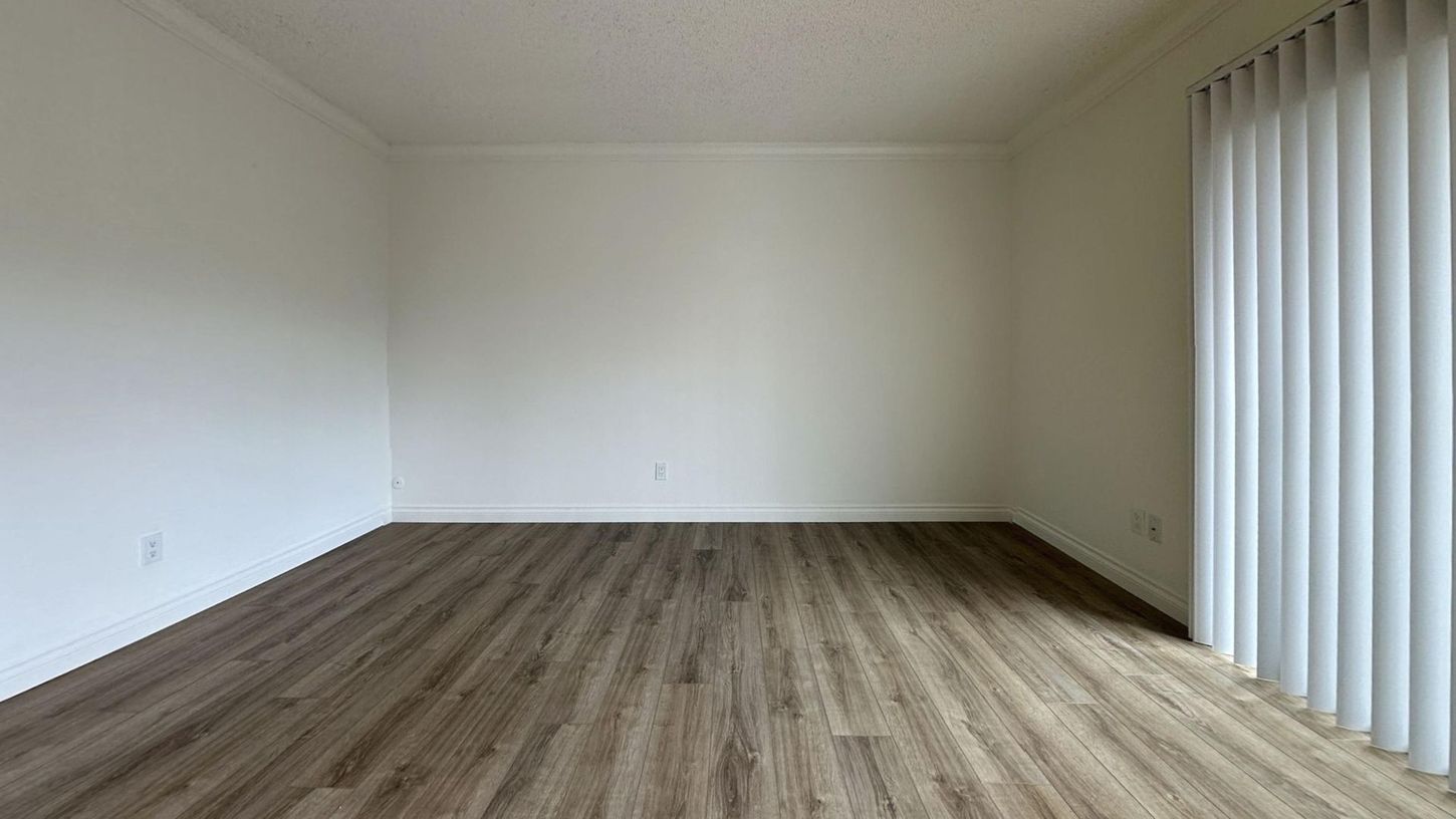 Empty room with white walls, wood-look flooring, and vertical blinds.