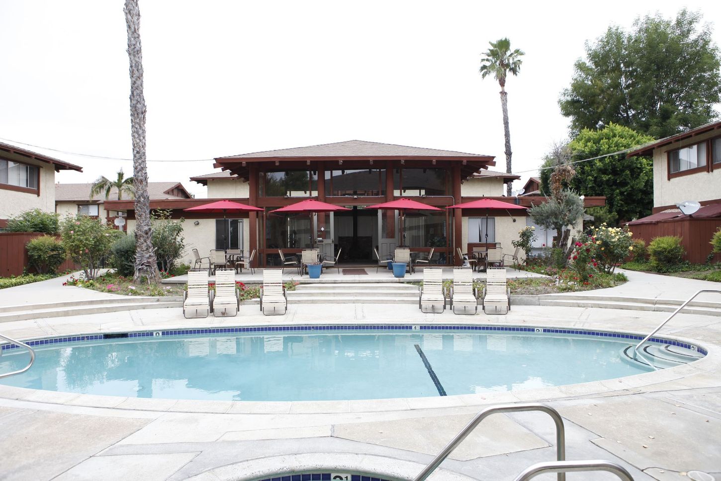 Swimming pool with lounge chairs, building with red trim, and palm trees.