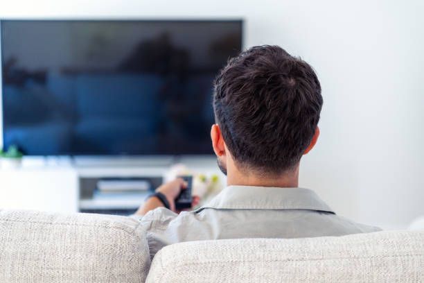 A man is sitting on a couch watching television.