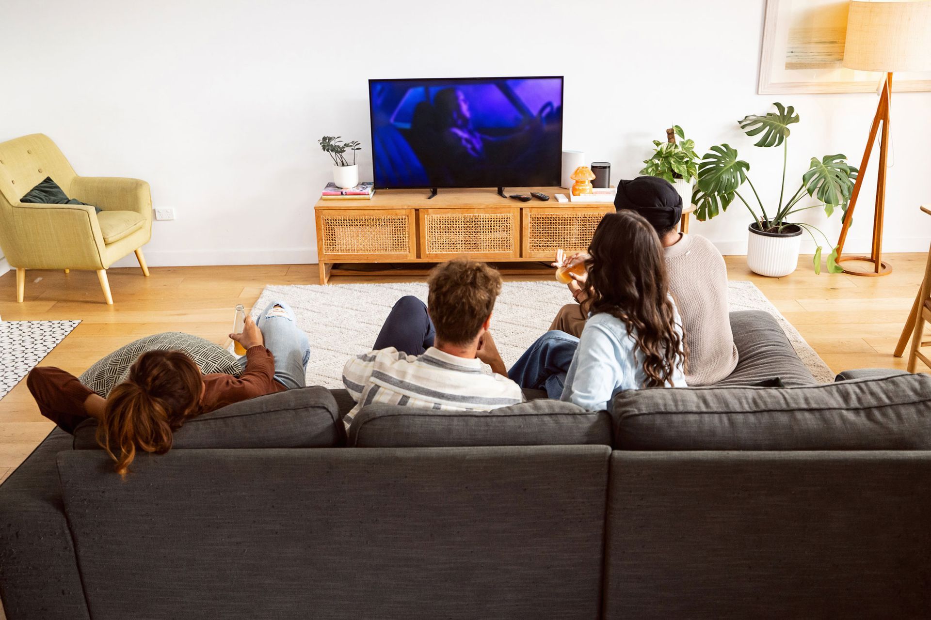 A group of people are sitting on a couch watching a television.