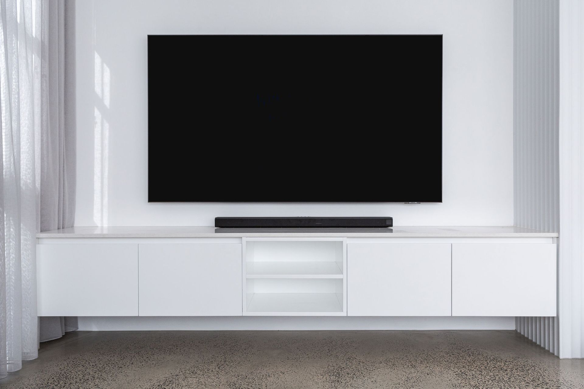 A flat screen tv is mounted on a white wall above a white entertainment center.