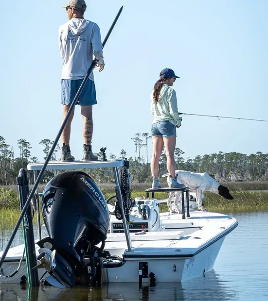 A man and a woman are fishing on a boat with a dog.