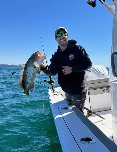 A man is standing on a boat holding a large fish.