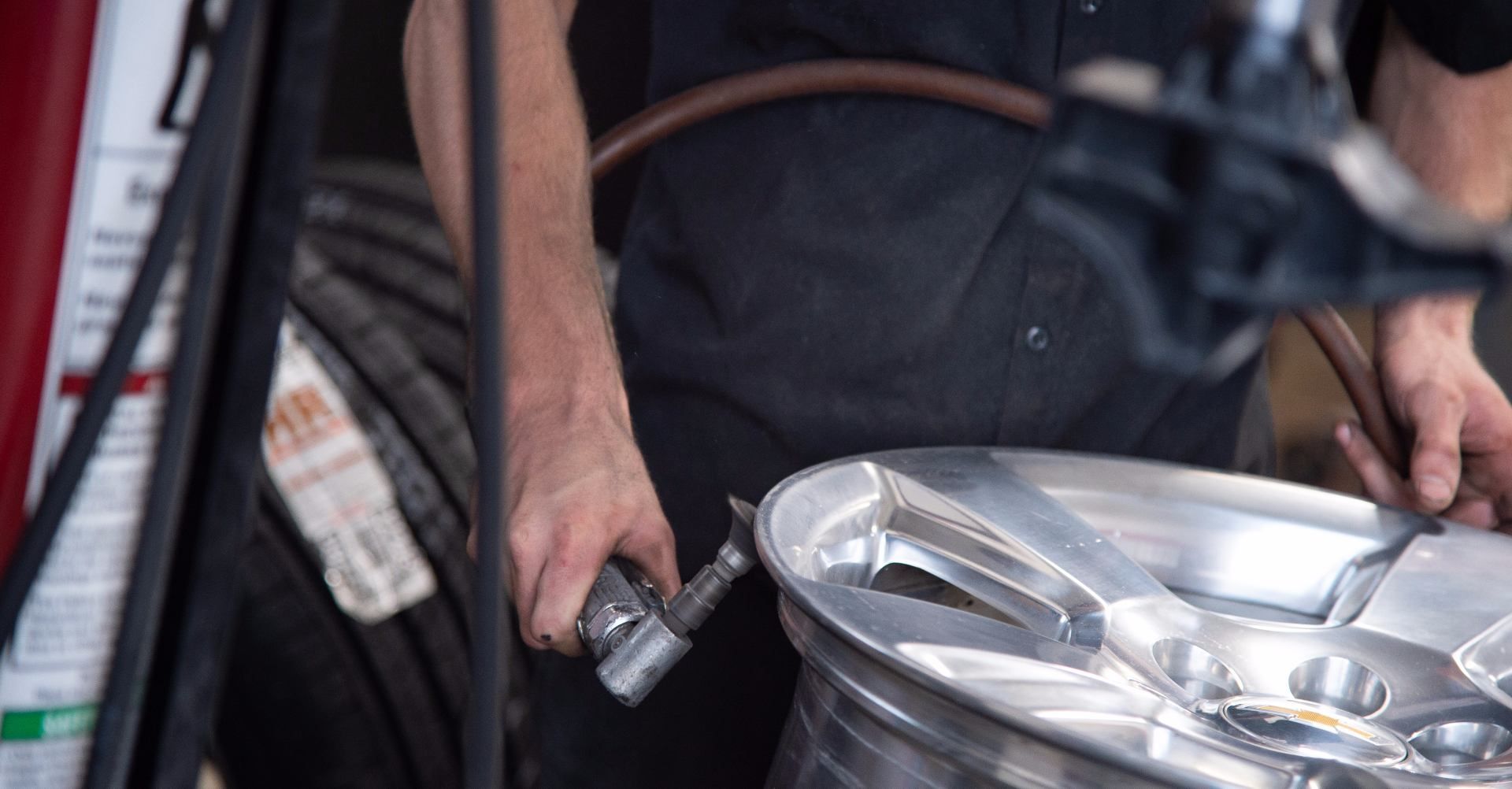 Mechanic using a tool on a car rim, likely inflating a tire. Indoors, hands in focus. | RX Automotive