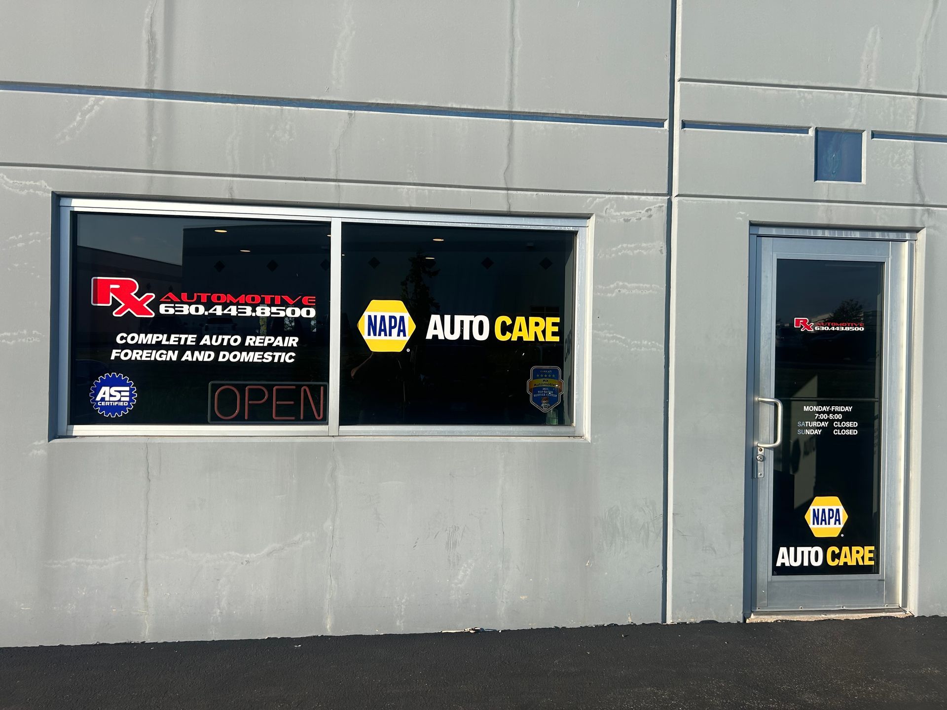 Exterior of an auto repair shop with signs for RX Autoworks, NAPA Auto Care, and OPEN. Gray building. | RX Automotive