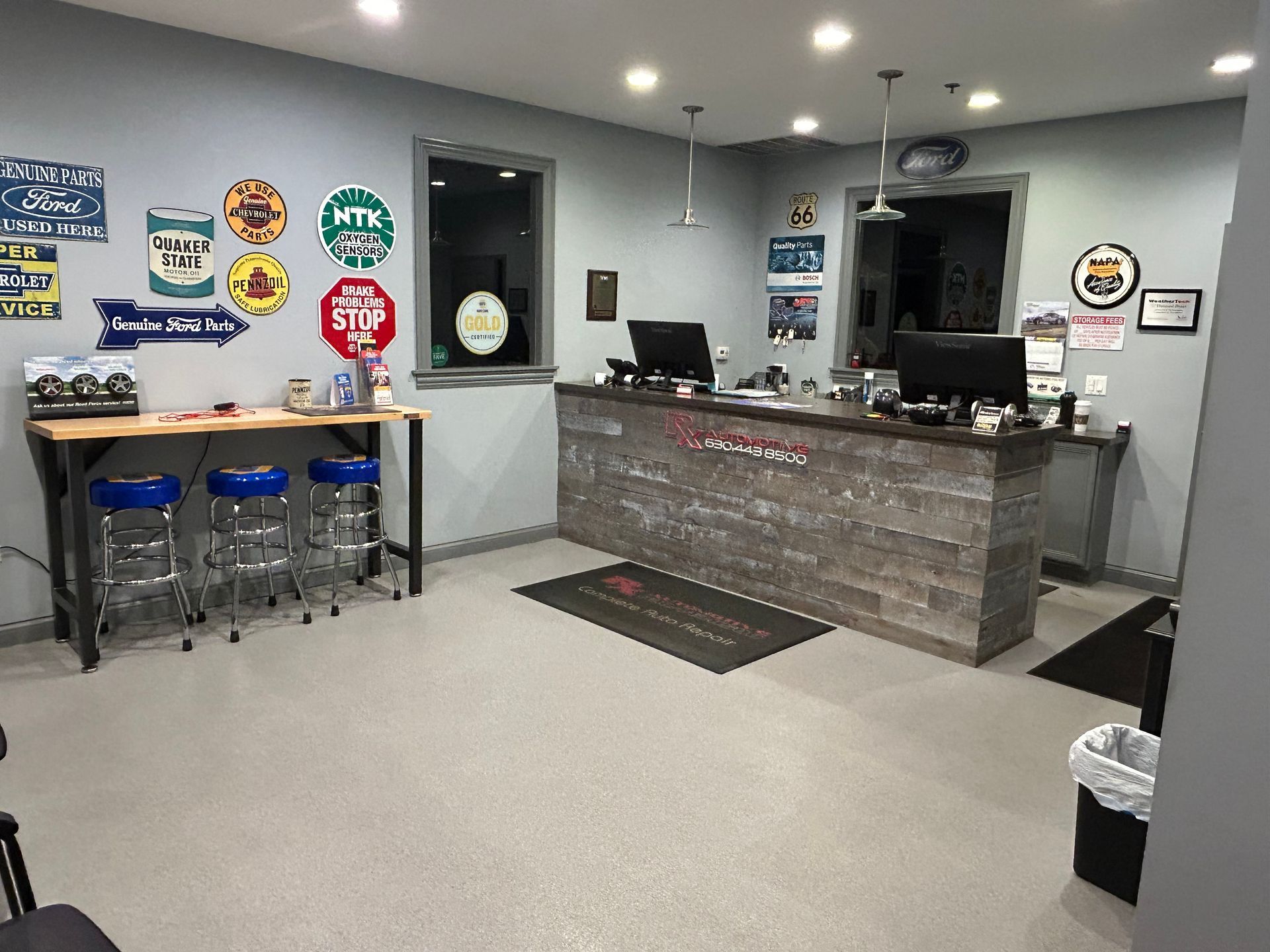 Auto repair shop office with reception desk, stools at a table, and wall decor. | RX Automotive
