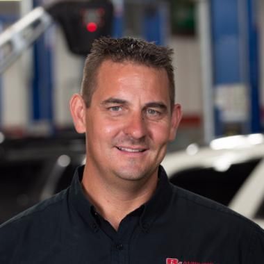 Man with short brown hair, wearing a black shirt, smiling in an auto repair shop - the owner | RX Automotive