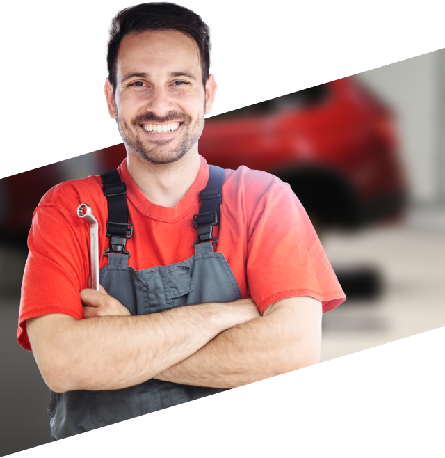 Smiling mechanic with arms crossed, holding a wrench, wearing a red shirt and gray overalls, in a garage with a red car. | RX Automotive