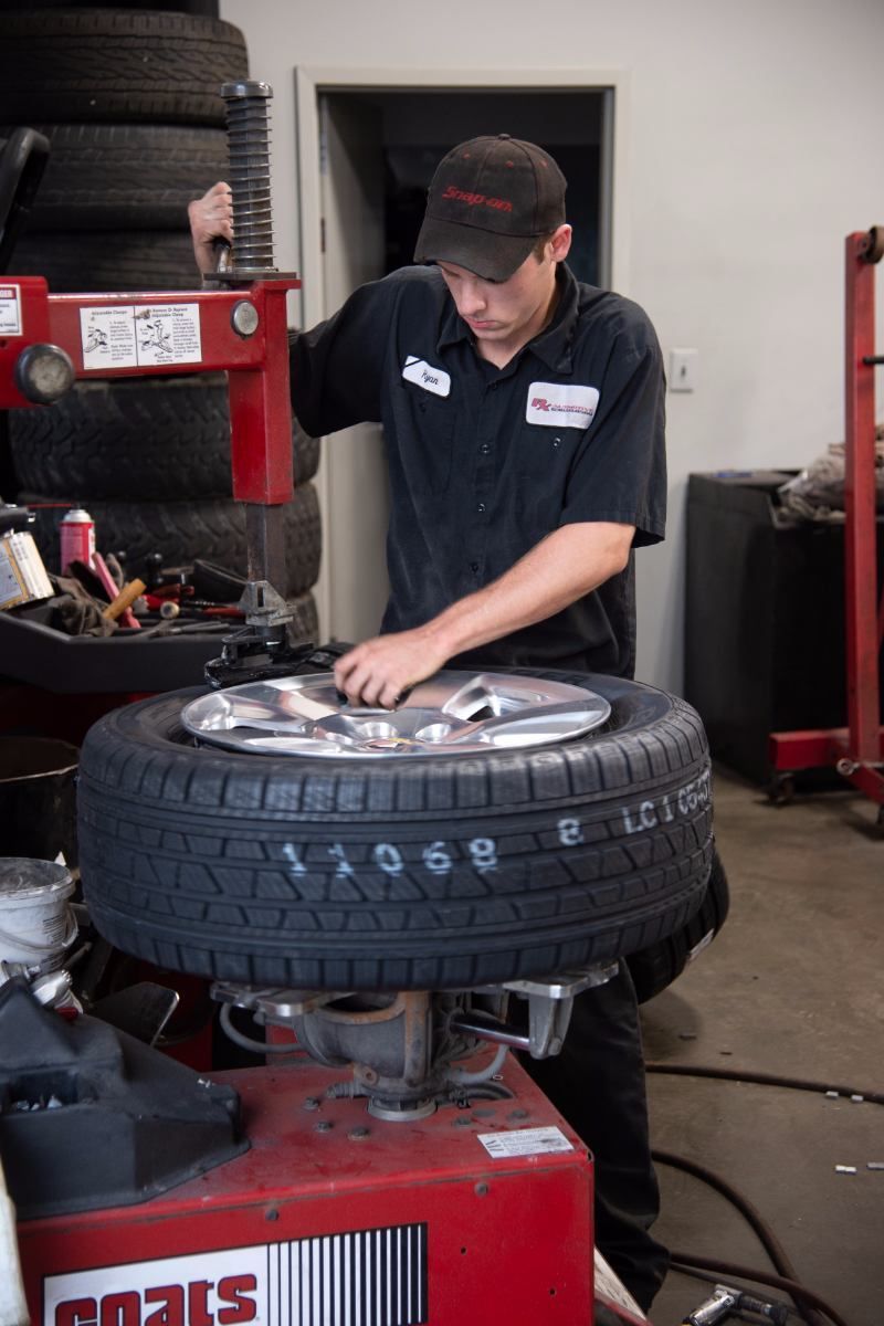 A mechanic in a black uniform works on a tire using a red machine in a shop. | RX Automotive