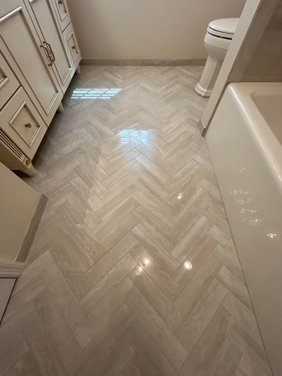 A bathroom with a herringbone tile floor and a toilet.