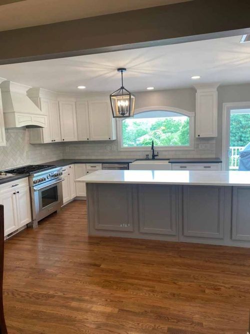 A kitchen with white cabinets , stainless steel appliances , hardwood floors and a large island.