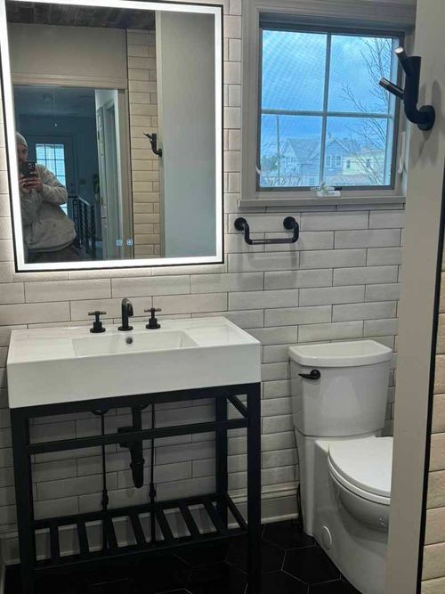 A bathroom with a sink , toilet , mirror and window.