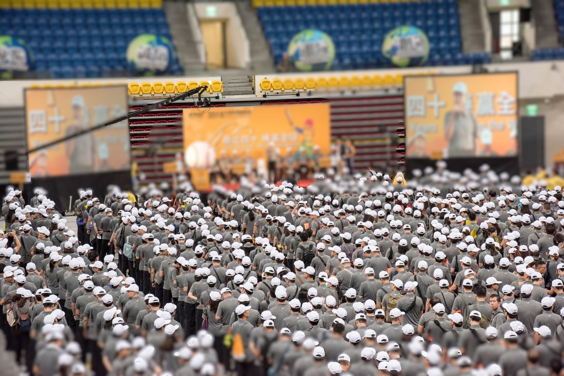 一大群戴著帽子的人面朝一個裝有揚聲器的舞台，很可能是競技場上的活動。