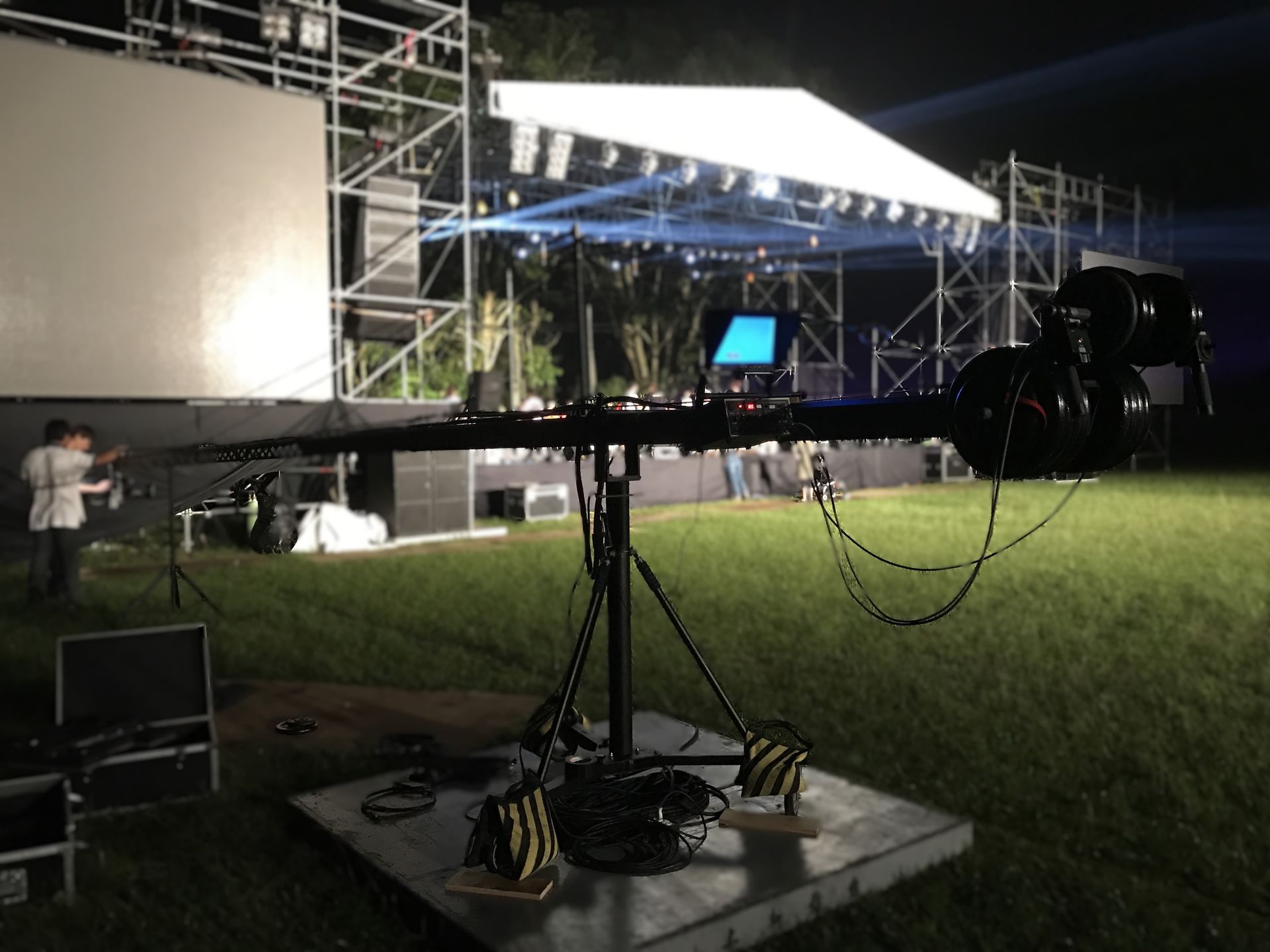 夜晚，攝影吊架架設在草地上，背景有舞台和燈光。